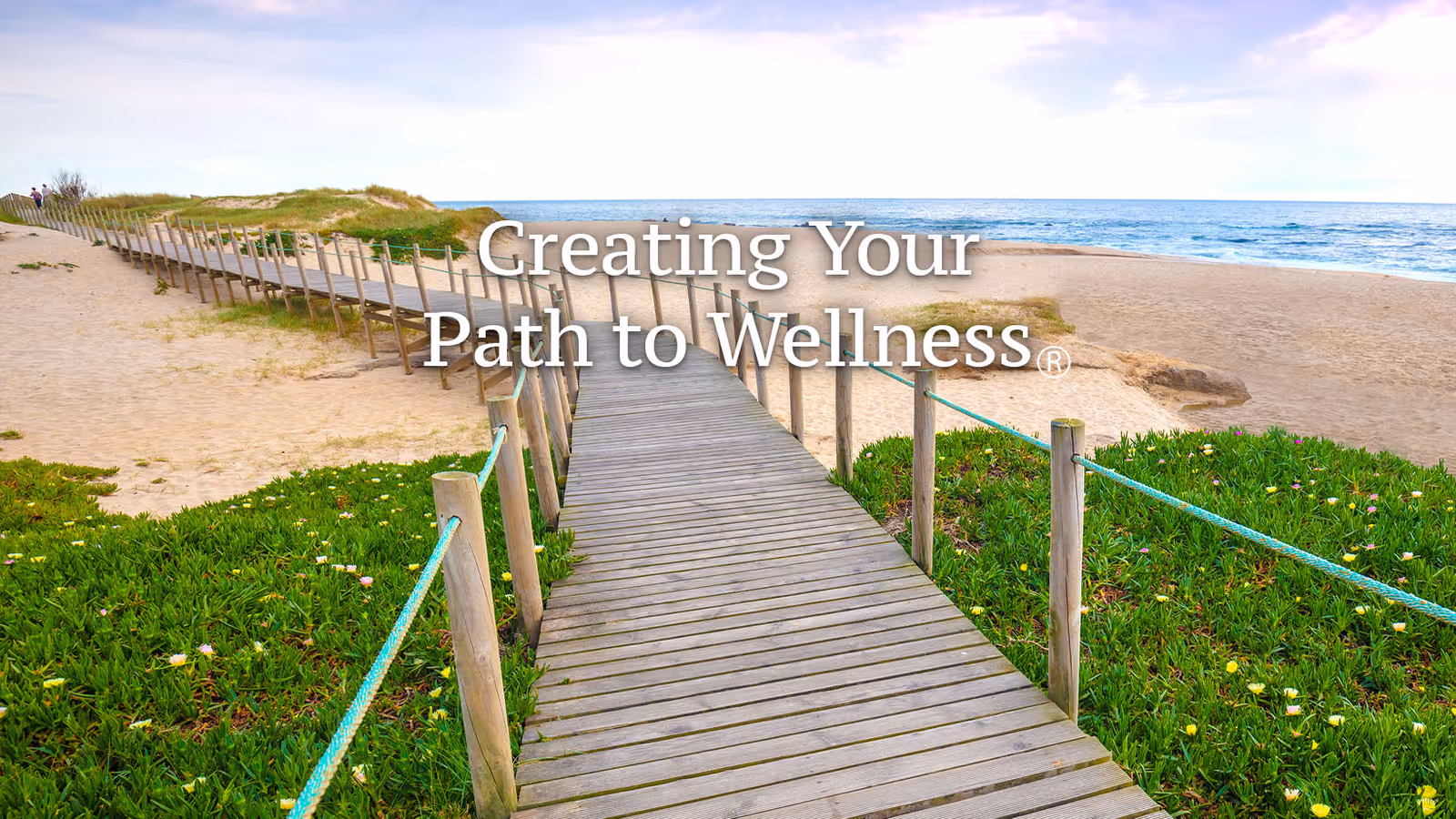 Wooden boardwalk through dunes toward a sunny beach and ocean.