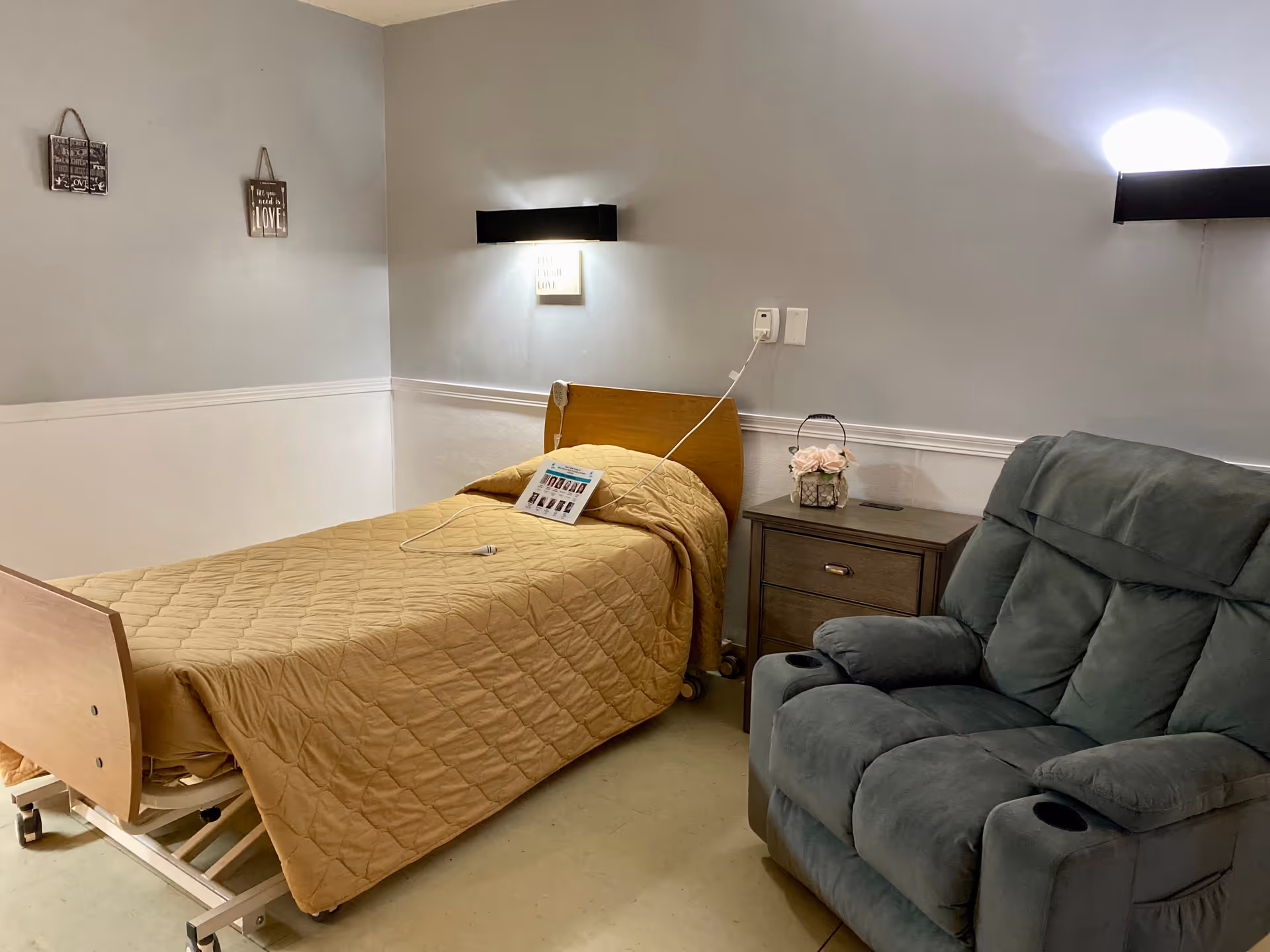 An interior resident bedroom with an adjustable bed, nightstand, and plush recliner.