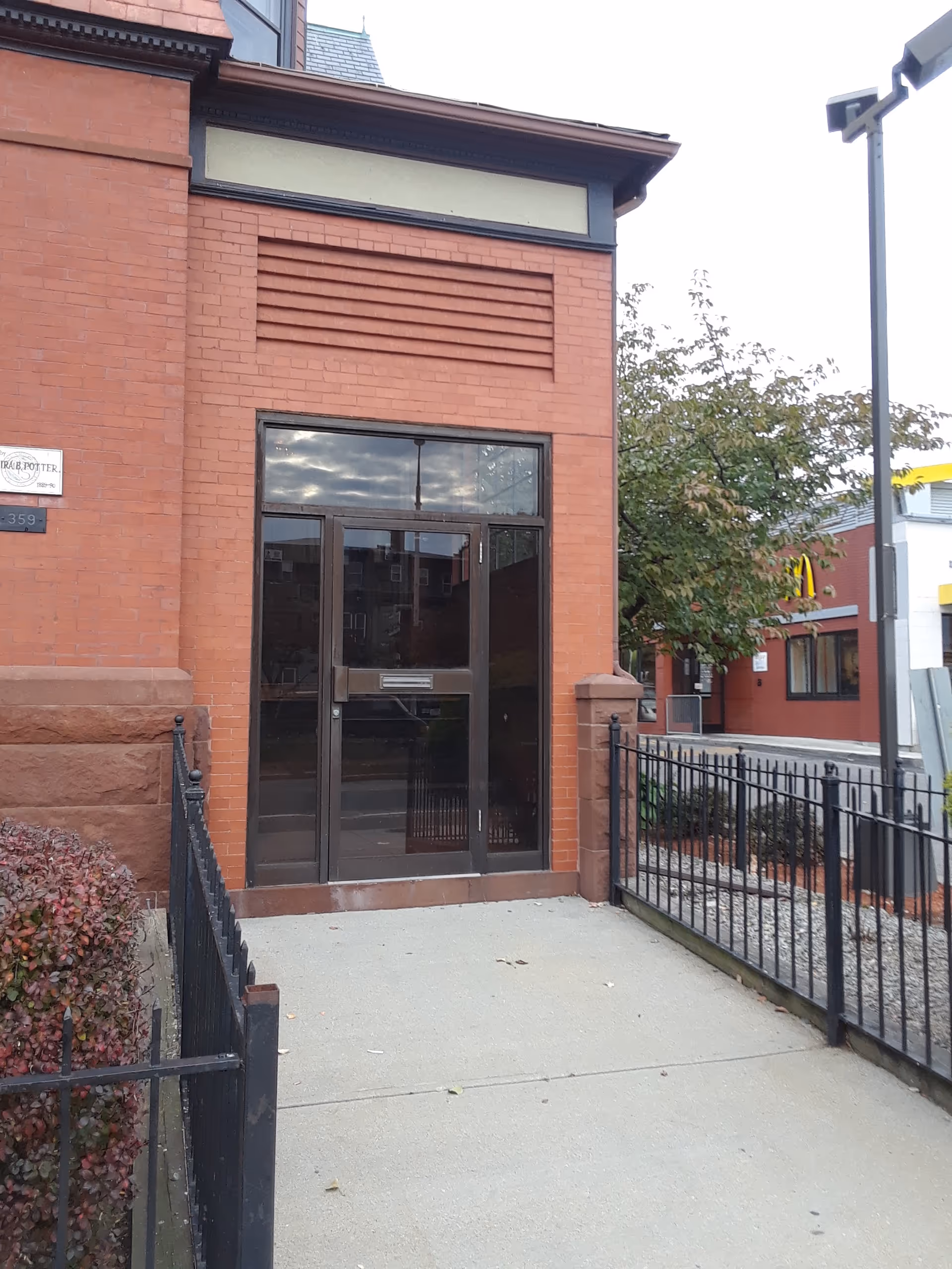 Brick building entrance with glass doors, metal frame, and fenced walkway.