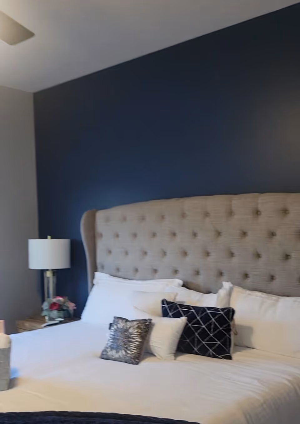 A neatly made bedroom with an upholstered tufted headboard, white sheets, and a nightstand lamp.