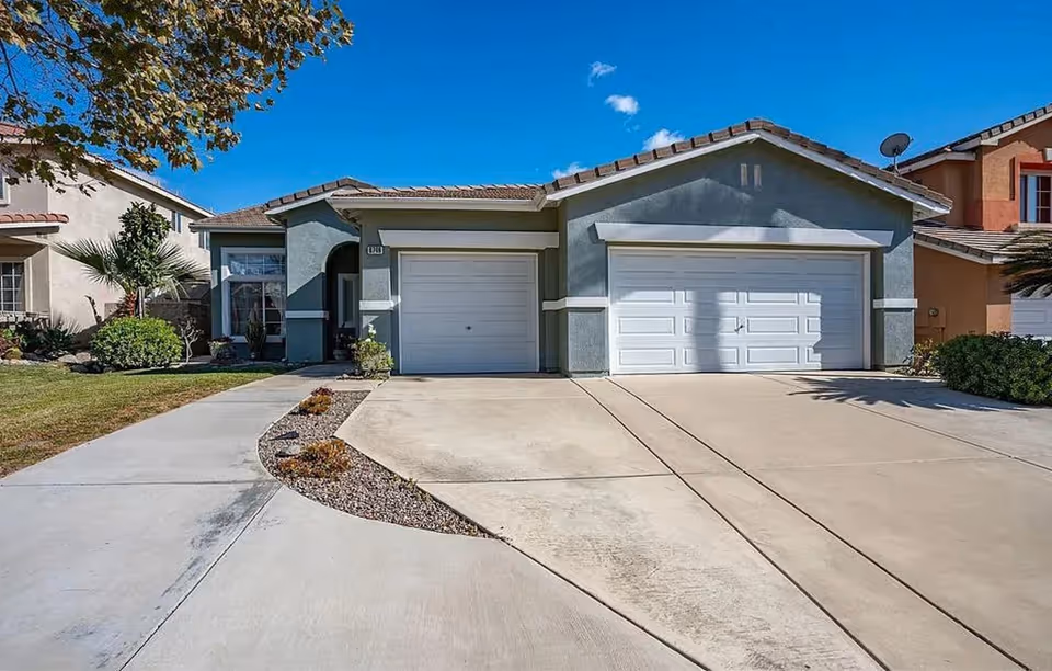 Front view of a two-car garage house with a curved driveway and desert landscaping.