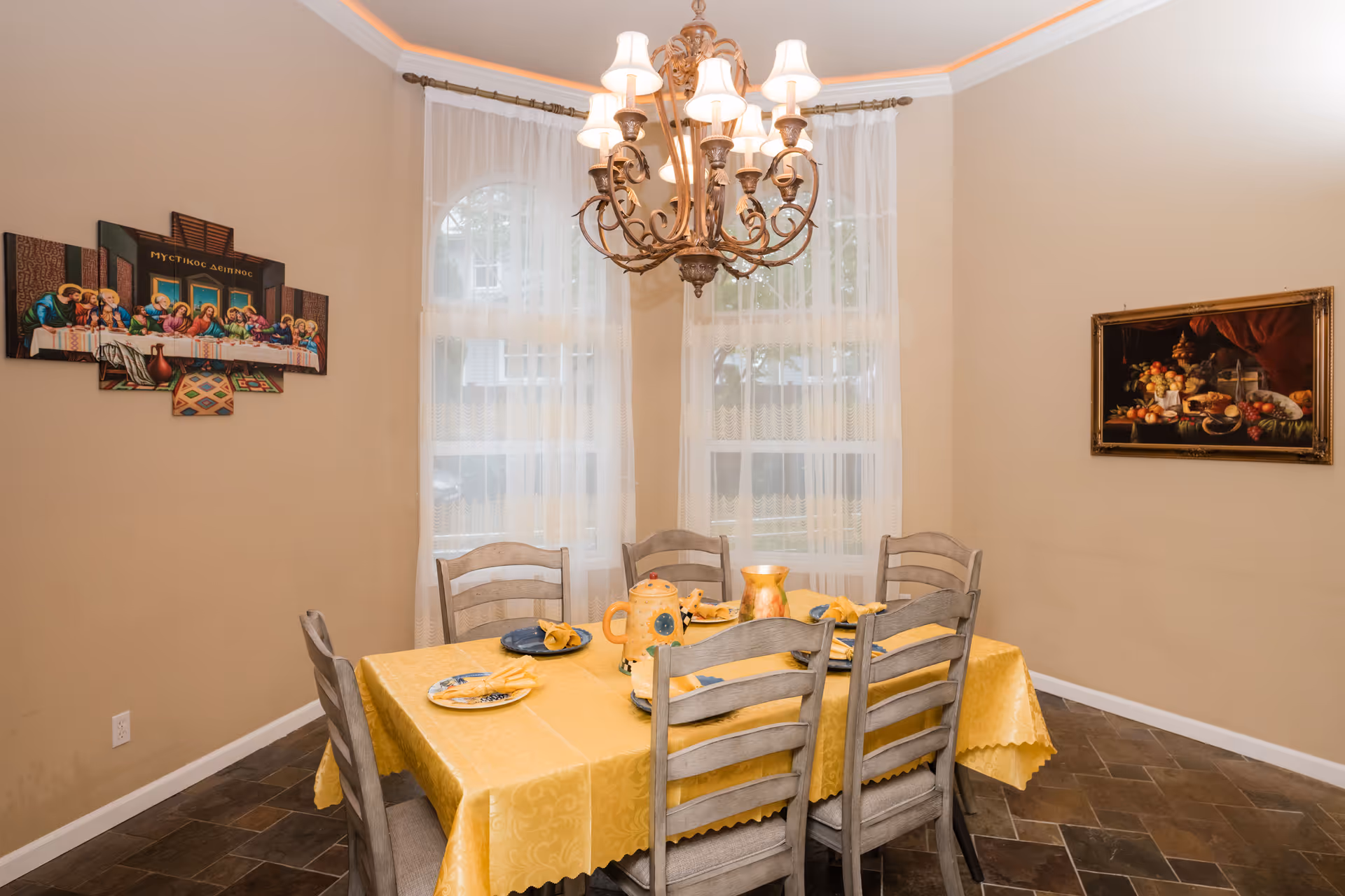 Dining room with a yellow-covered table, chairs, chandelier, and wall art.