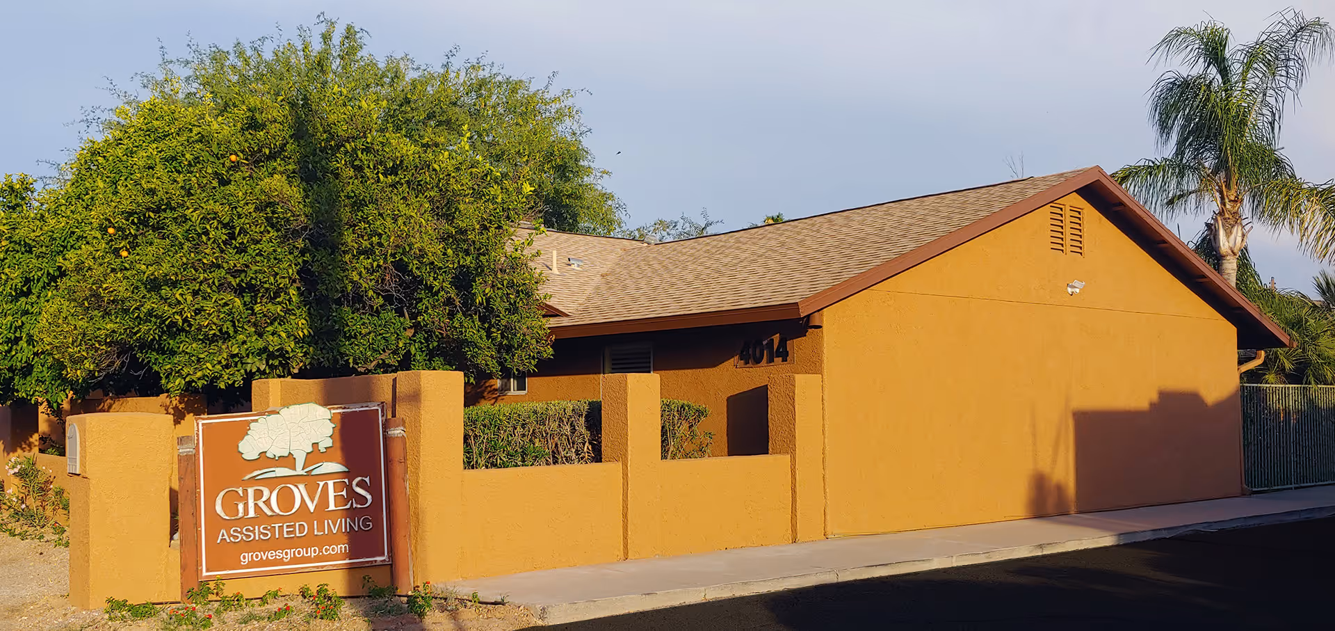 Front exterior of an orange stucco building with a 'GROVES Assisted Living' sign, trees, and a paved frontage.