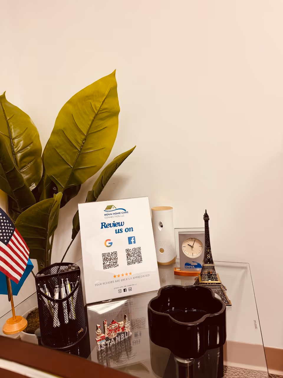 Desk area at Nova Home Care Connection with plant, flags, clock, Eiffel Tower model, review sign.