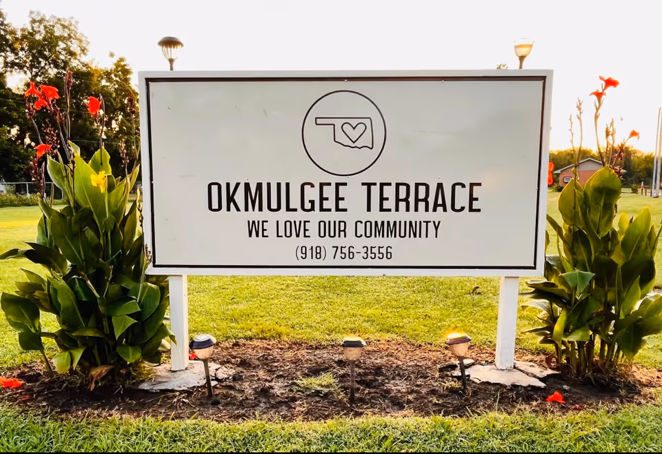 Outdoor sign for Okmulgee Terrace LLC on a grassy lawn with plants.