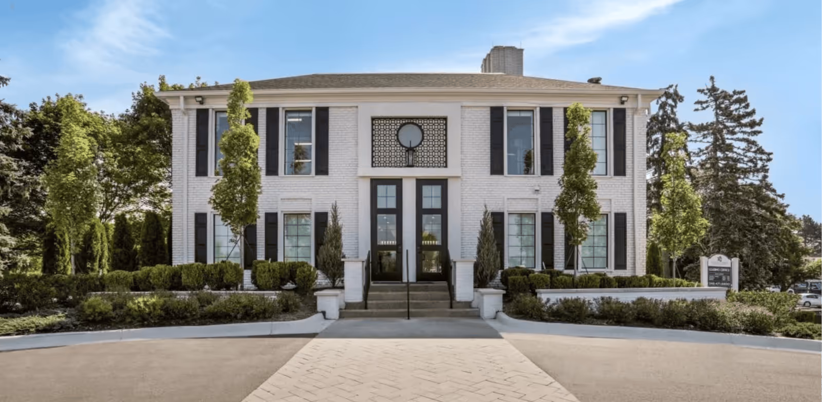 White brick senior living facility with black shutters and a centered entrance on a landscaped front