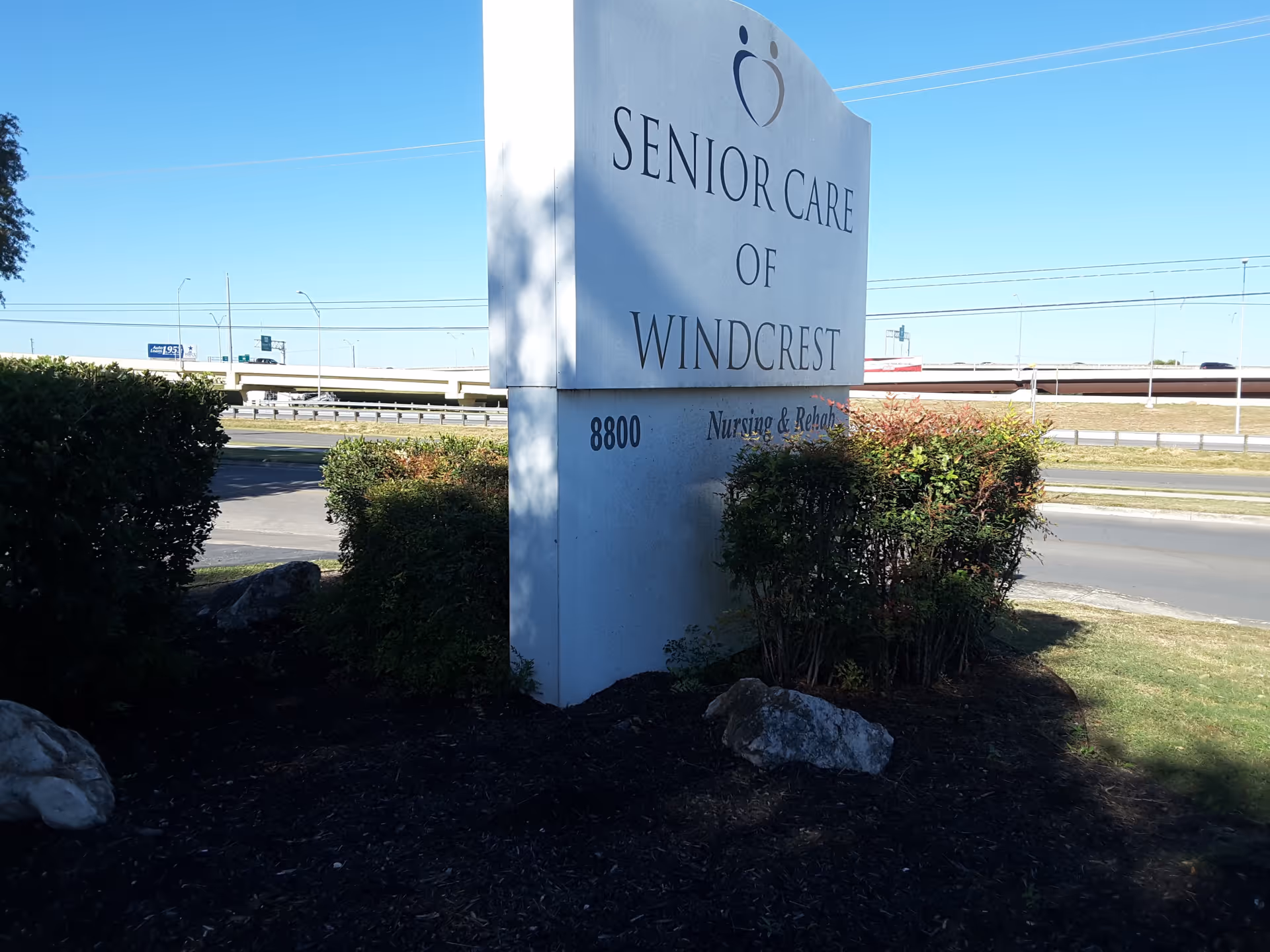 Tall white sign reading 'Senior Care of Windcrest' near a roadway