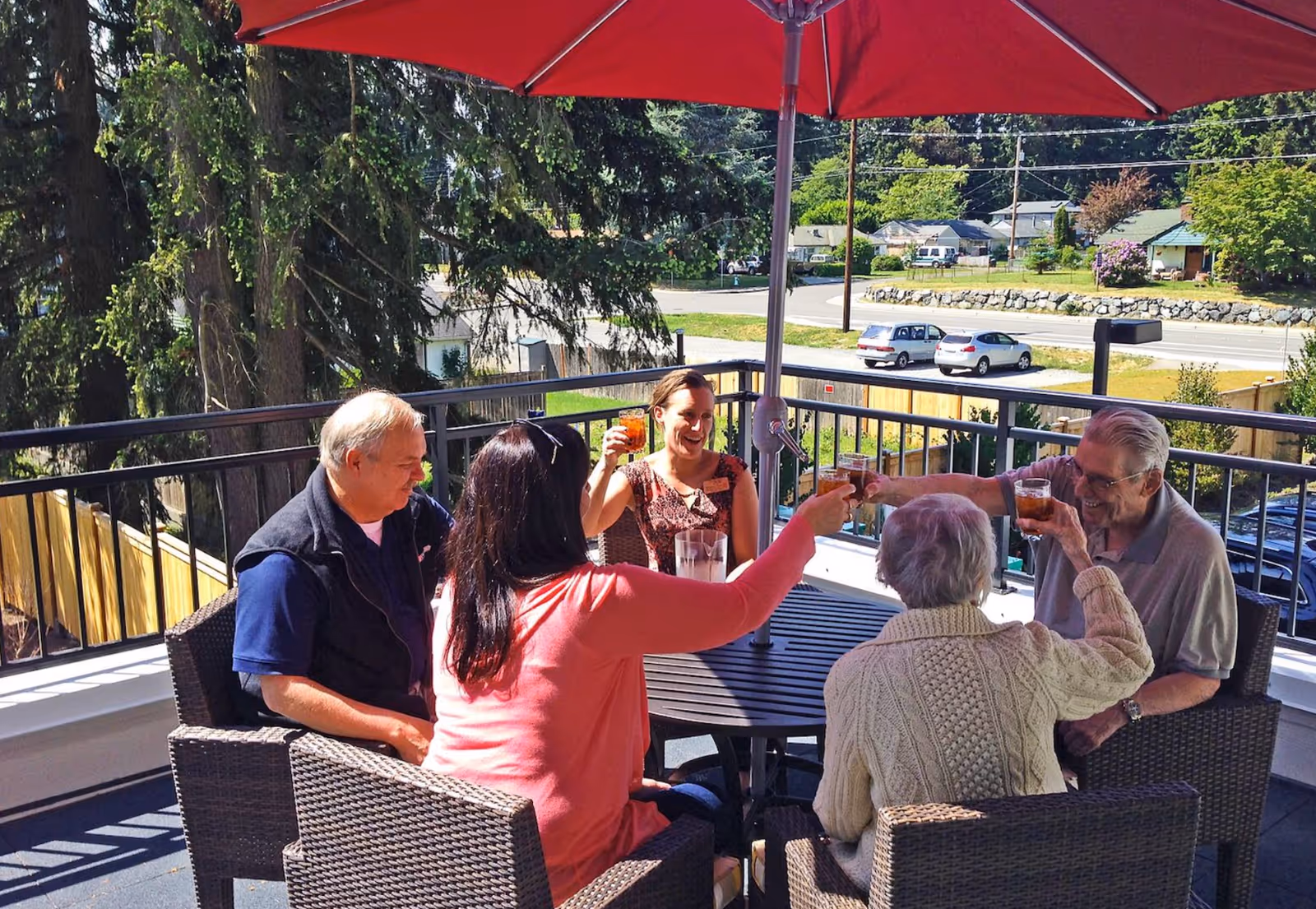 Group of seniors toasting drinks at an outdoor balcony table.