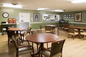 Dining area in a senior facility with round tables, wooden chairs, and green walls.
