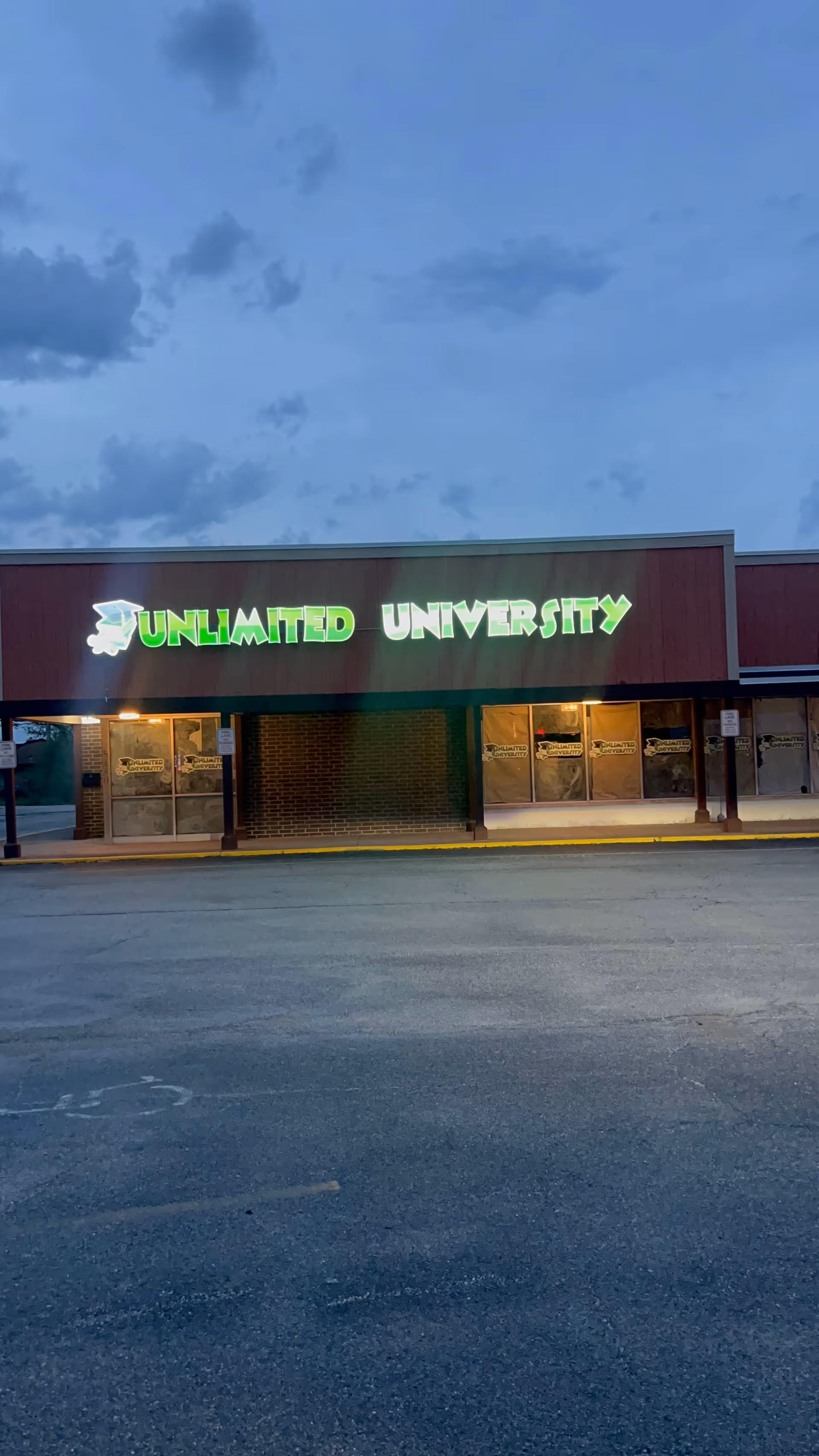 Exterior storefront with brown facade and a bright green 'Unlimited University' sign over empty parking lot.