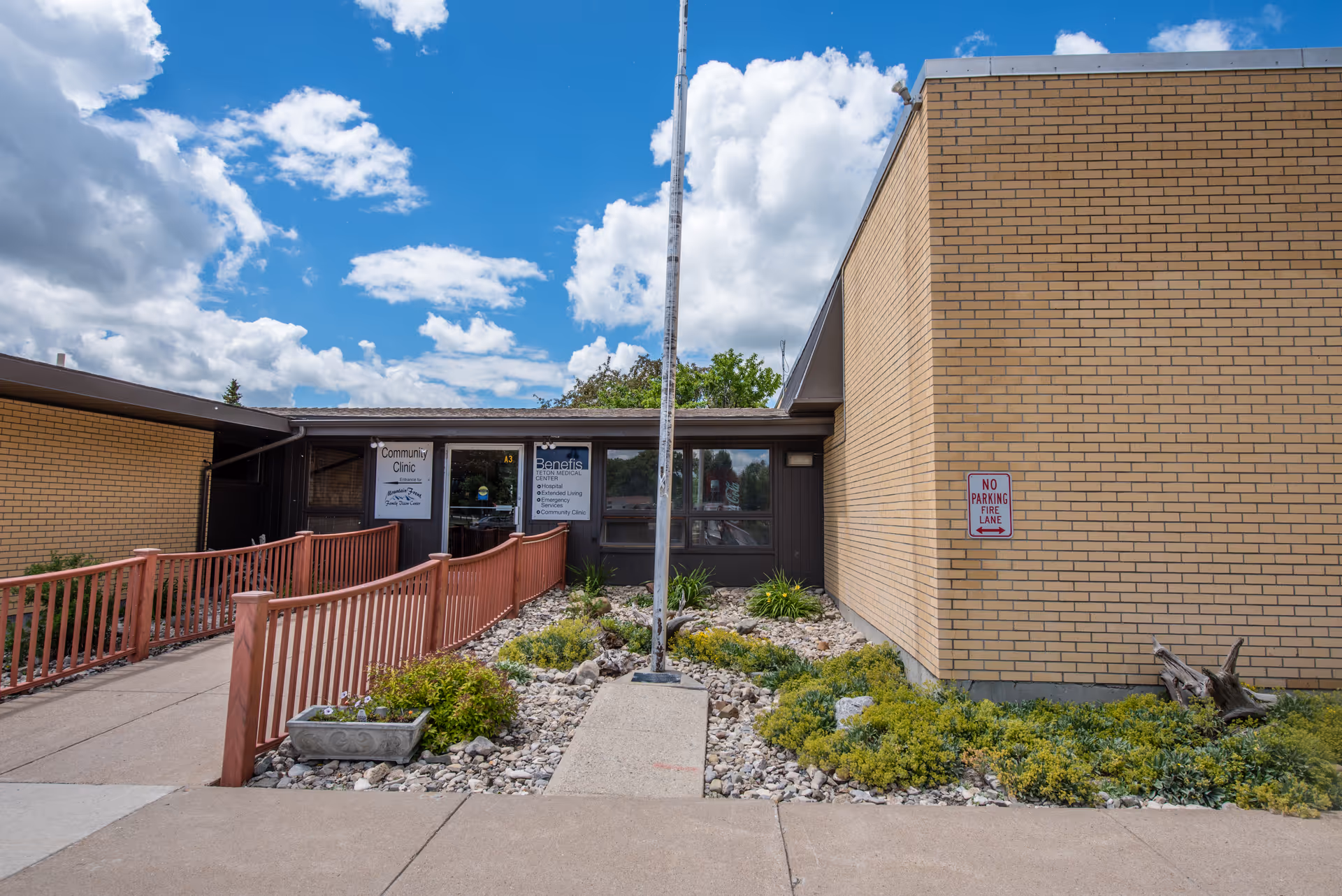 Exterior view of a brick medical facility entrance with a ramp and landscaped walkway.