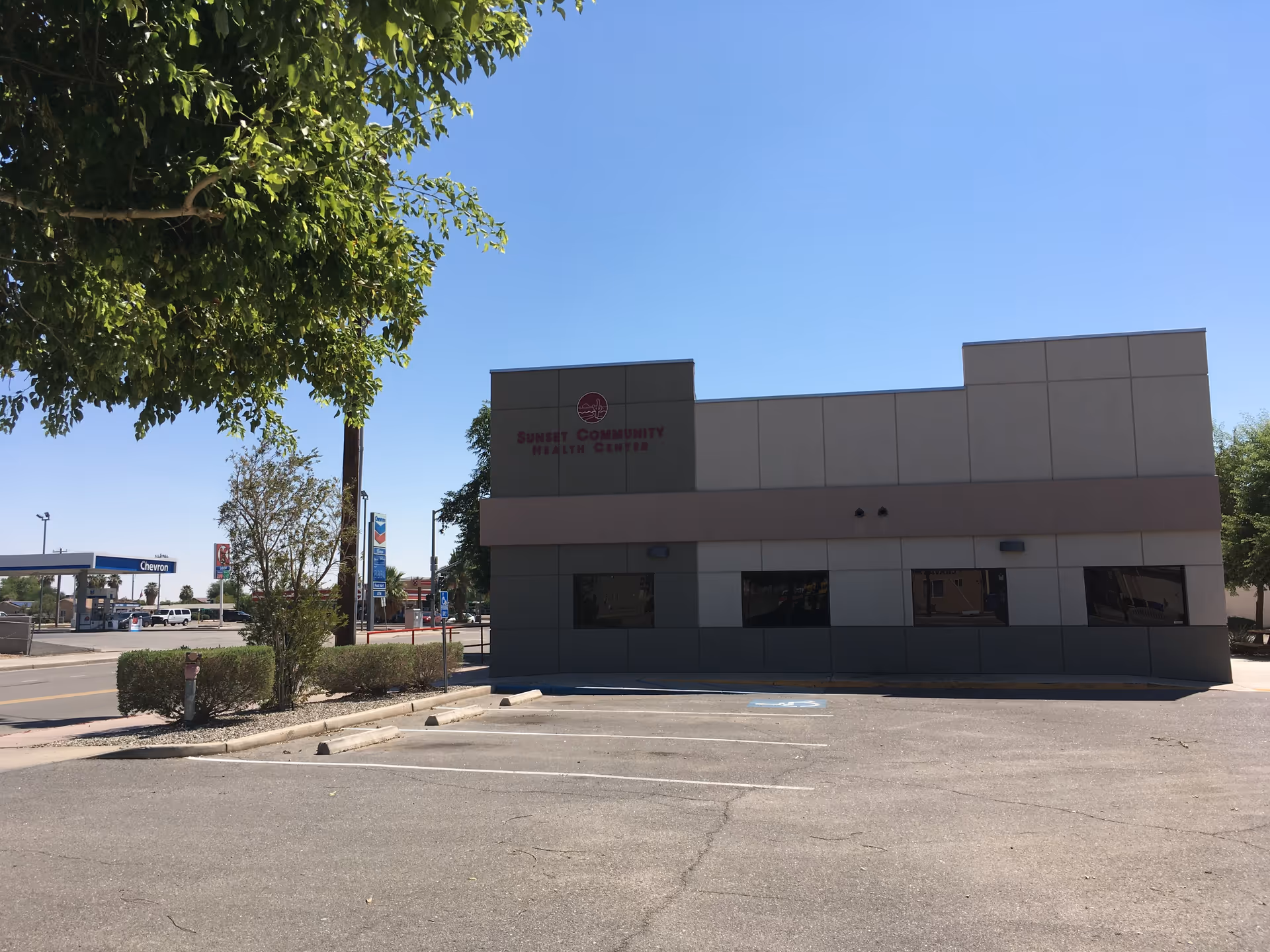 Front view of Sunset Health Inc building with parking lot and blue sky.
