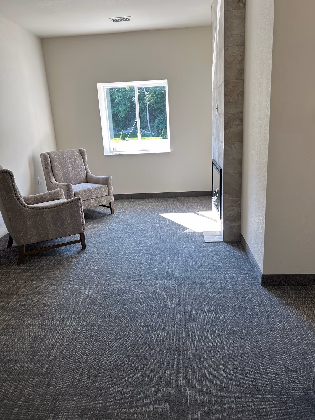 A small, empty lounge with two gray armchairs beside a window.