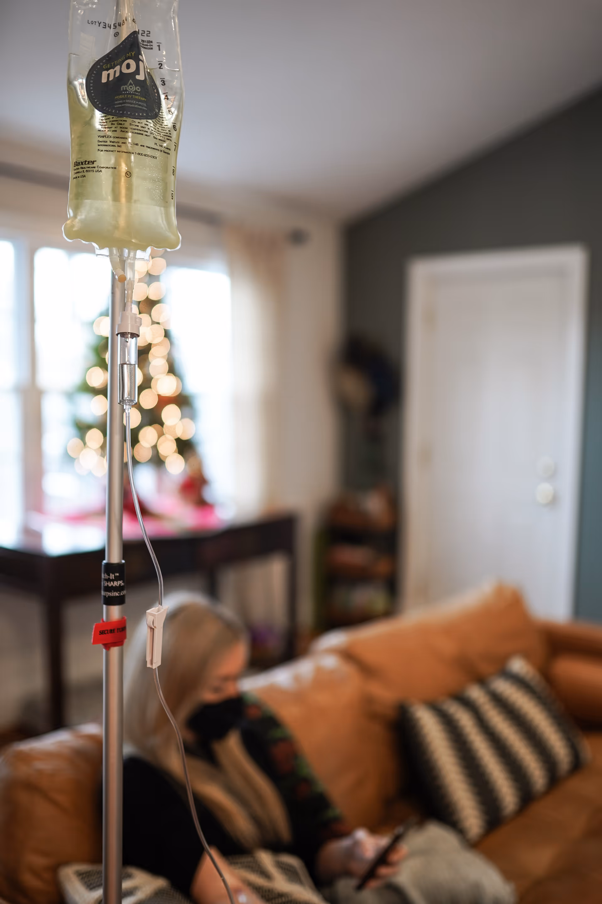 An IV bag on a pole in living room with a resident seated on a couch