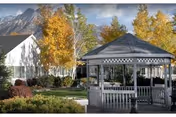 A white gazebo sits in a landscaped outdoor area with autumn trees and mountains.
