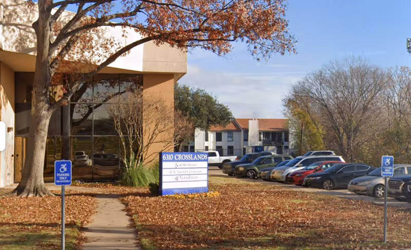 Exterior view of a senior care facility with a parking lot and autumn leaves.