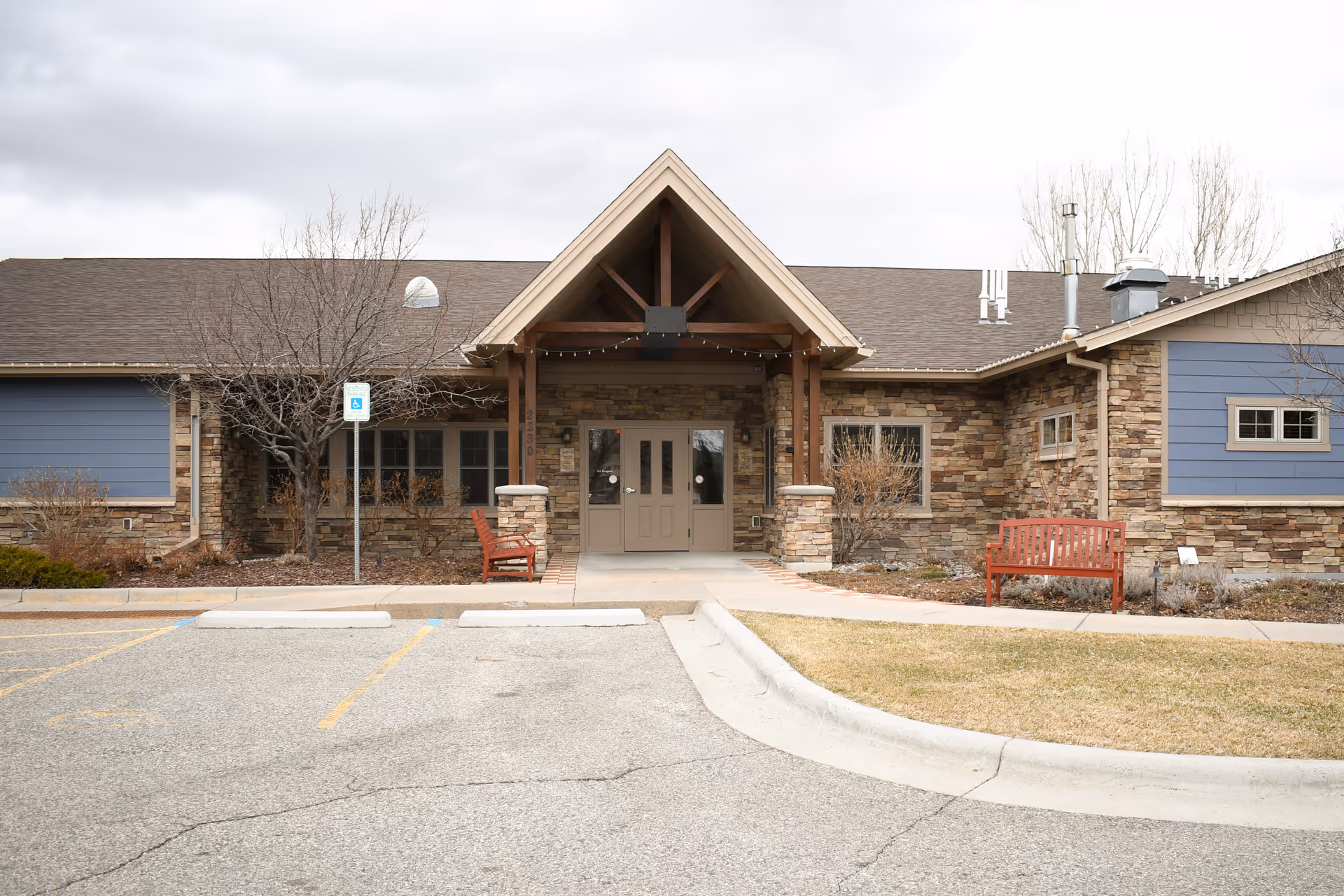 Front view of a stone and blue exterior senior living facility entrance with a wooden canopy.