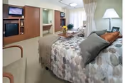 A cozy senior living bedroom with a patterned bedspread, seating area, and TV.