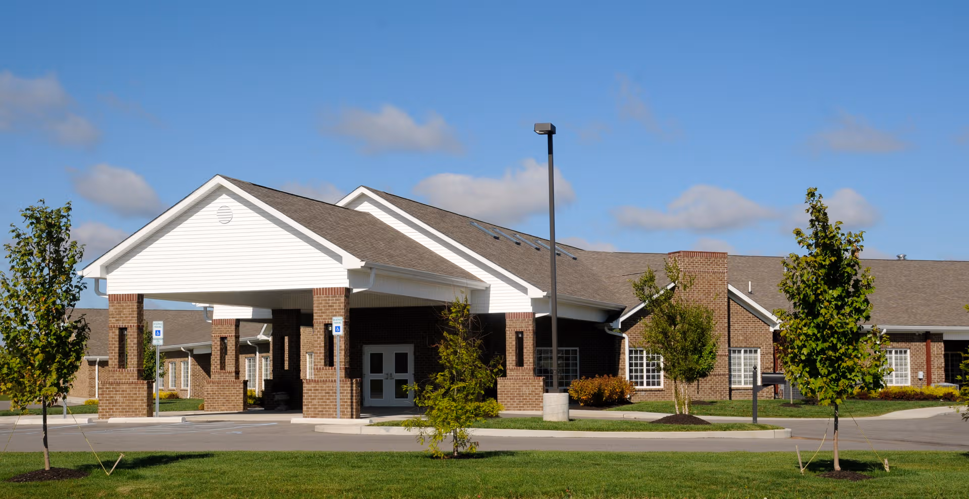 Front view of a senior living facility with a covered entrance and landscaped lawn.