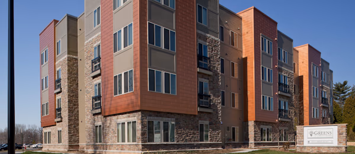 Exterior view of a modern multi-story senior living building with Greens sign