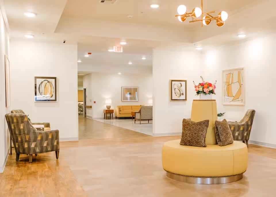 Bright senior living lobby with circular yellow seating, a flower vase, and contemporary art.