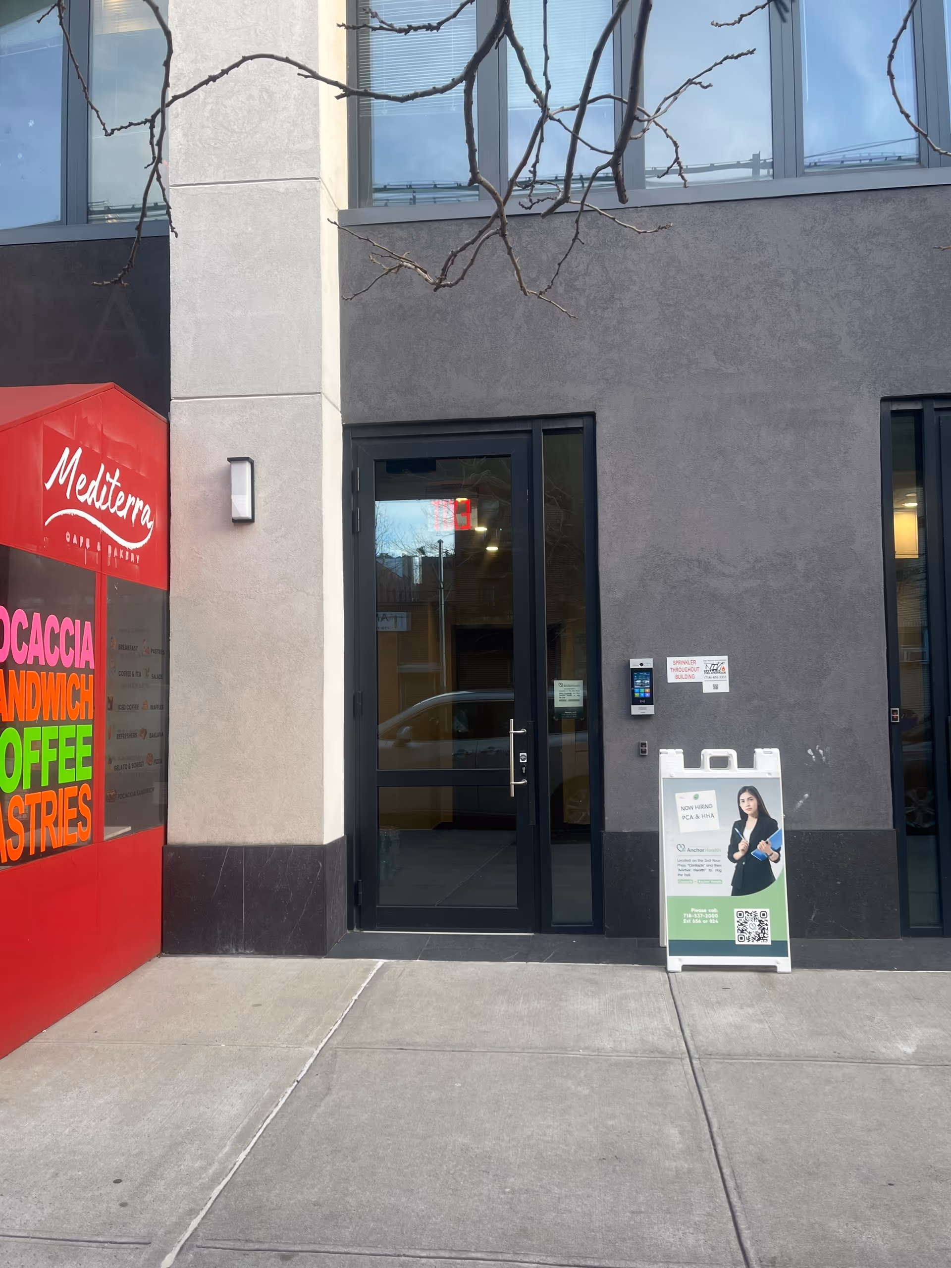 Street-level shot of a building entrance with glass doors and a red storefront on the left.