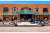 Brick-front entrance of Green Meadows Nursing & Rehabilitation Center with a green canopy and planters.