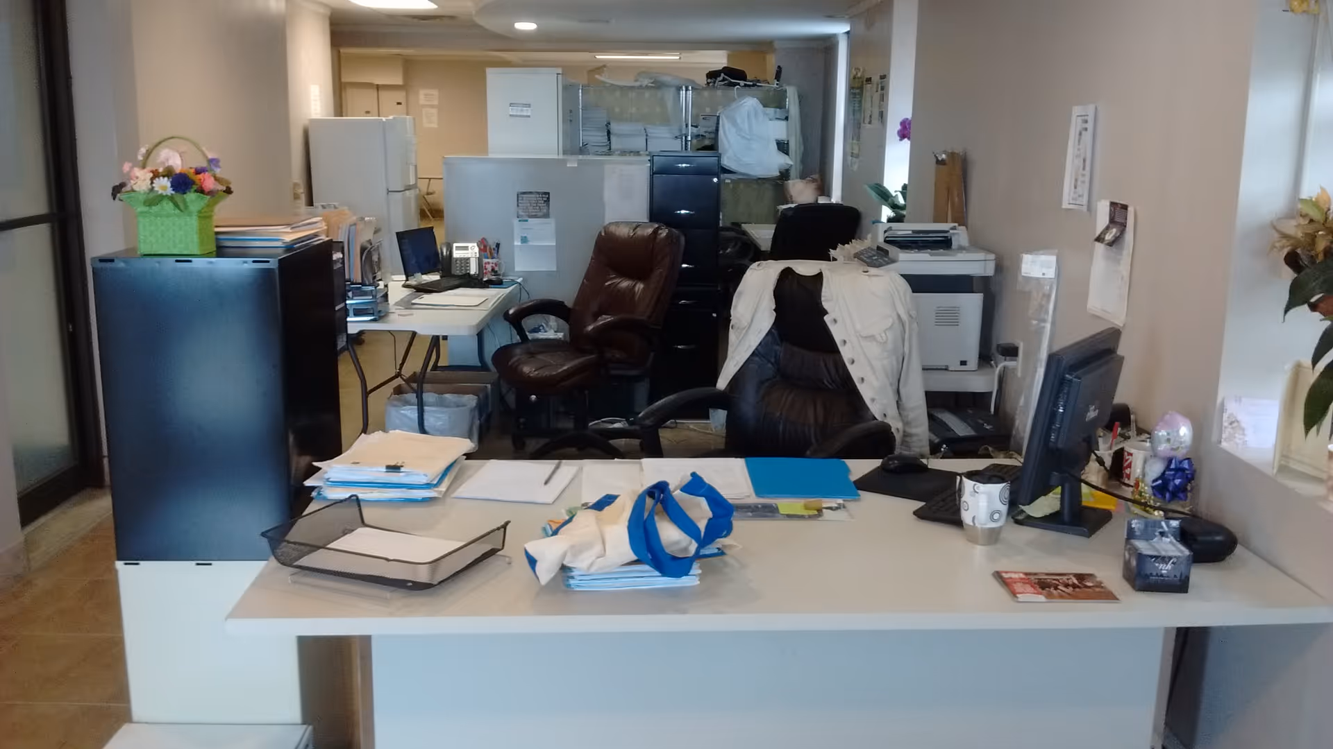 Office area with desks, chairs, computers, and paperwork inside a senior care facility.
