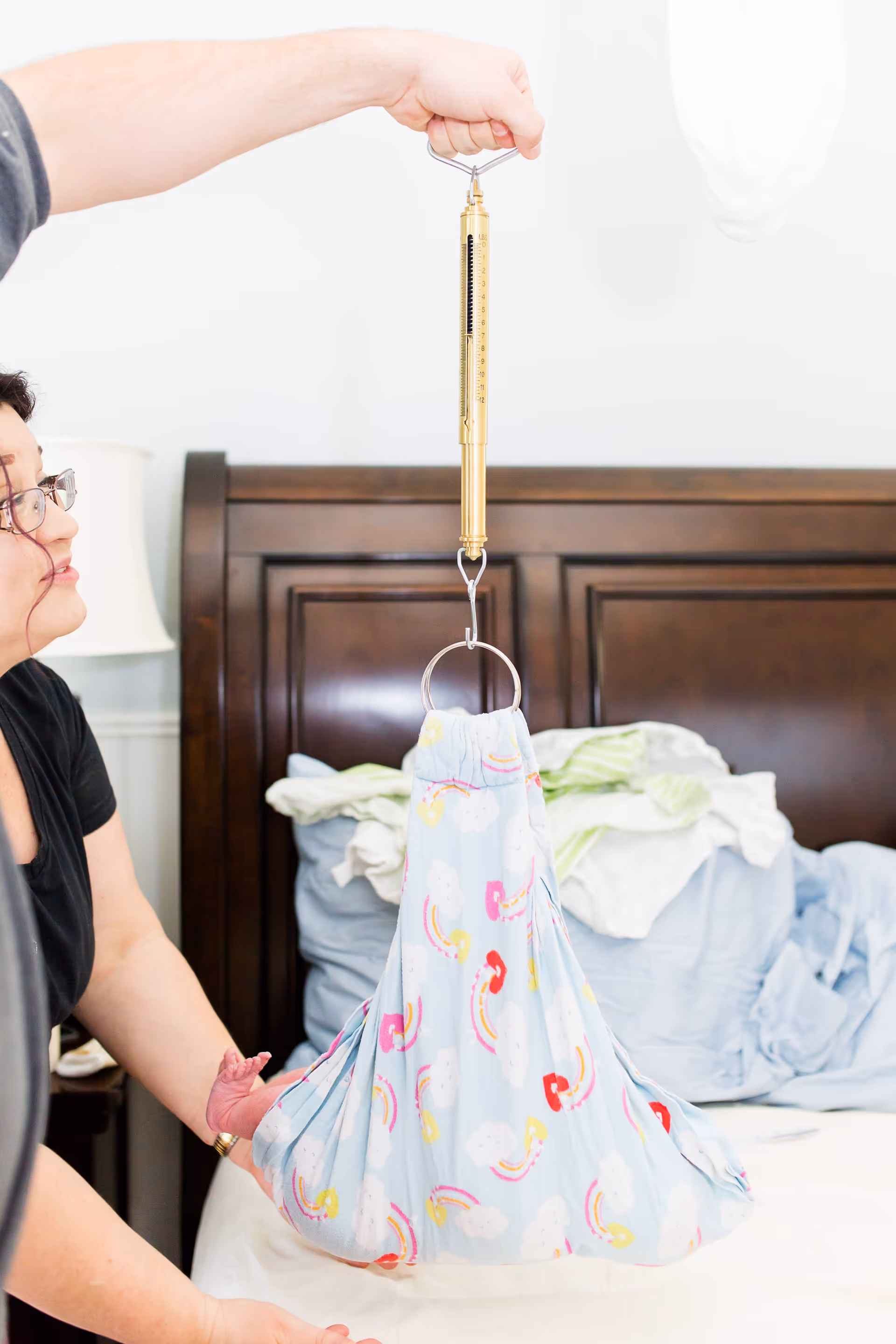 Caregiver uses a bed transfer sling and hoist over a dark wooden headboard.