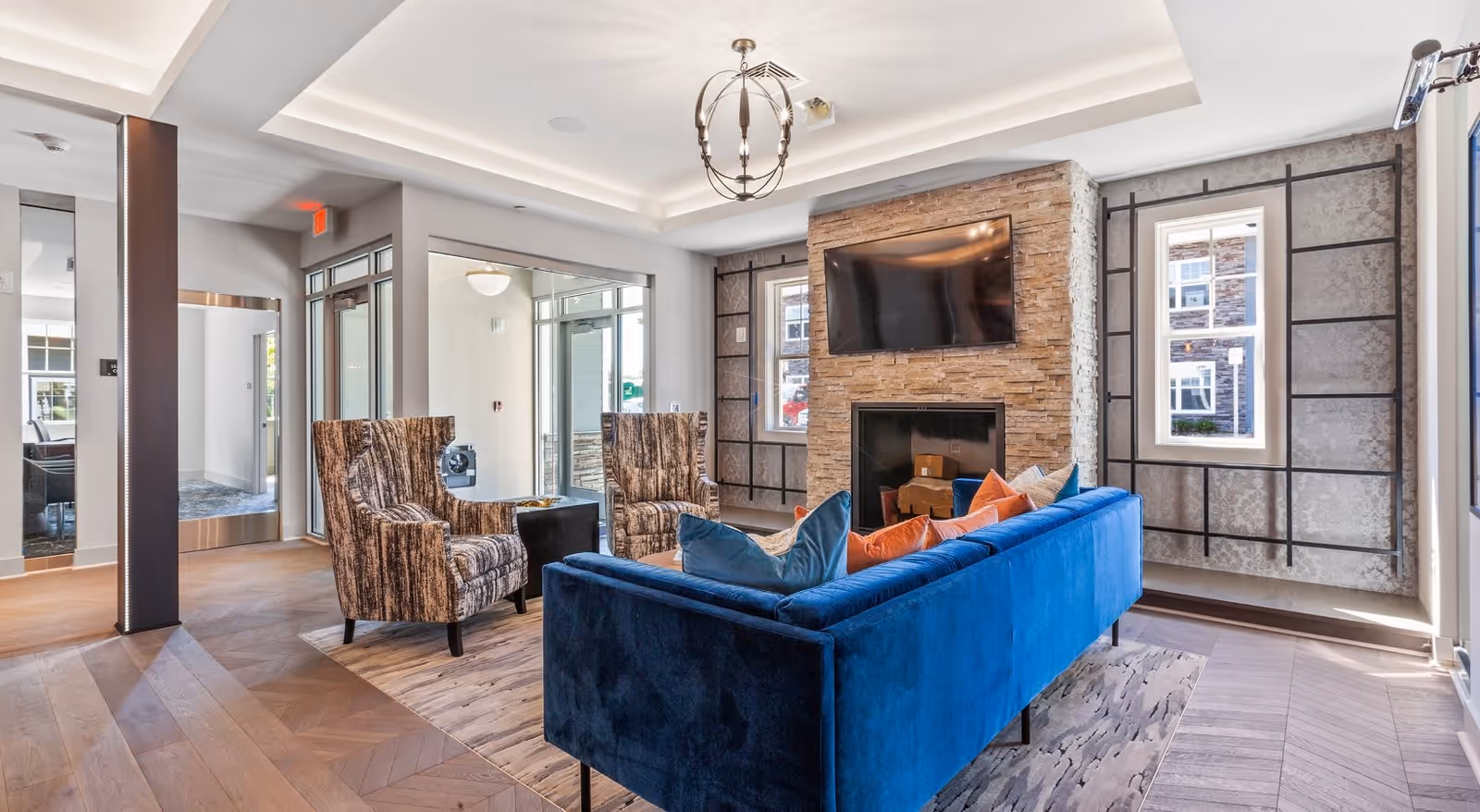 Modern lounge with a blue velvet sofa, patterned armchairs, a stone fireplace with wall-mounted TV, and large windows.