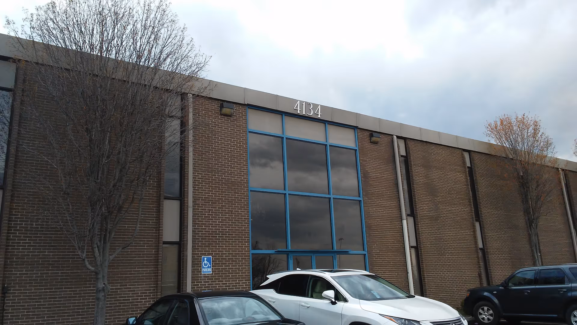 Brick facility exterior with blue-framed glass entrance and parked cars outside.
