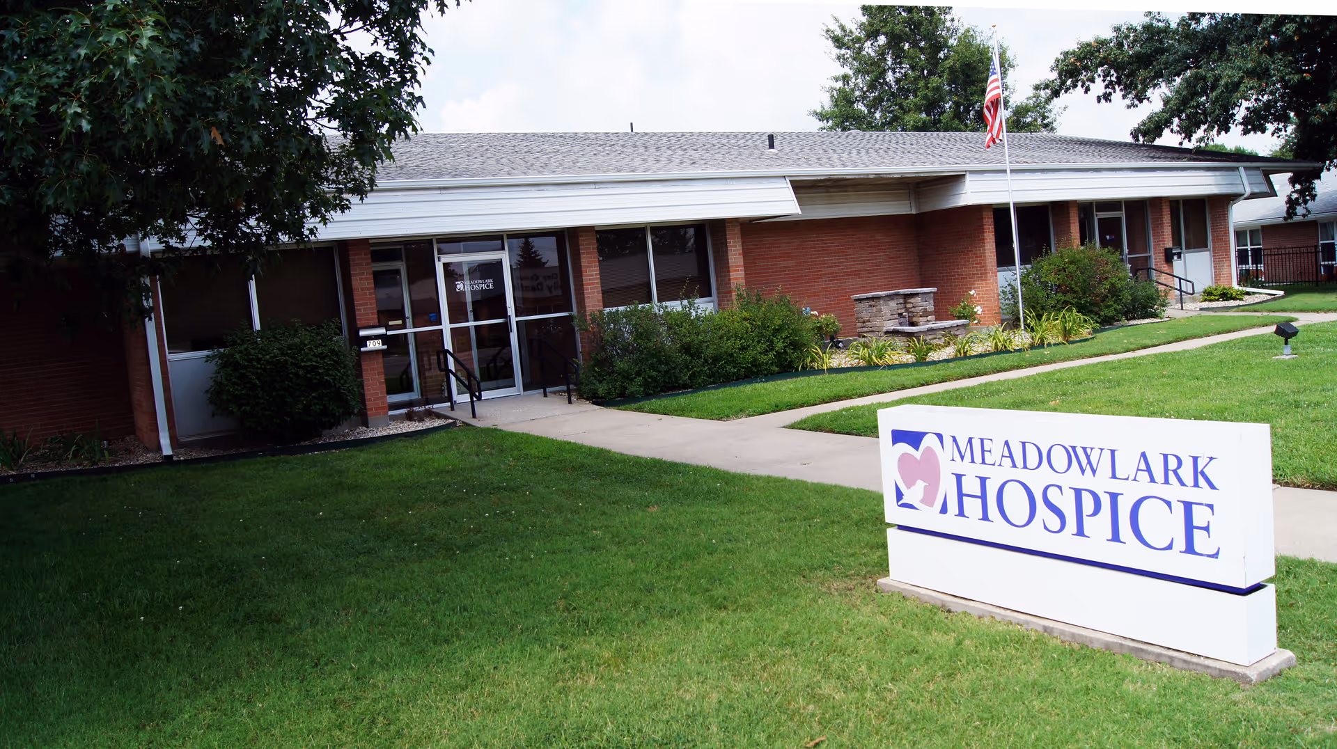 A single-story brick hospice building with a Meadowlark Hospice sign on a grassy lawn.