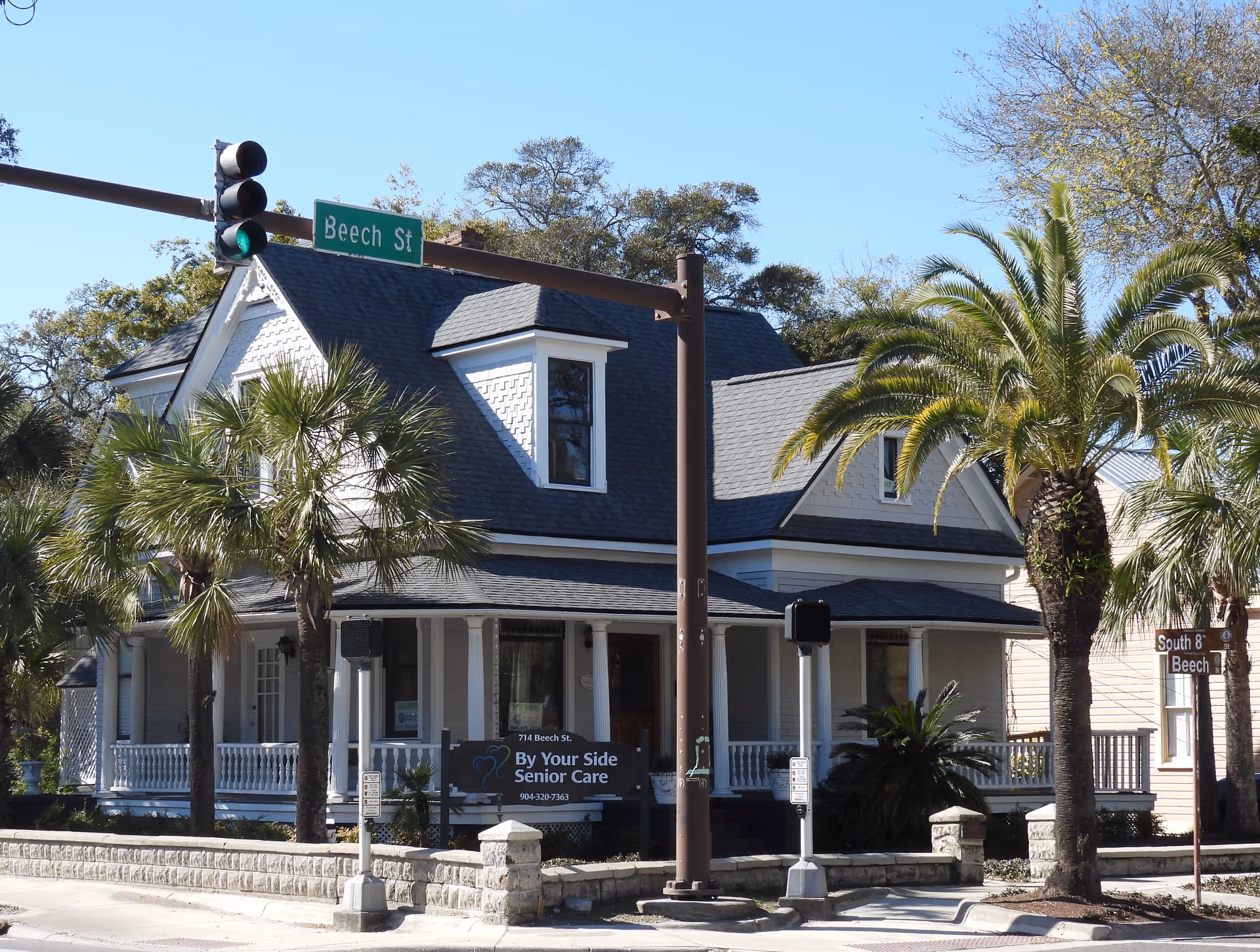 White, wooden senior care building with a porch, palm trees, and street sign at Beech Street.