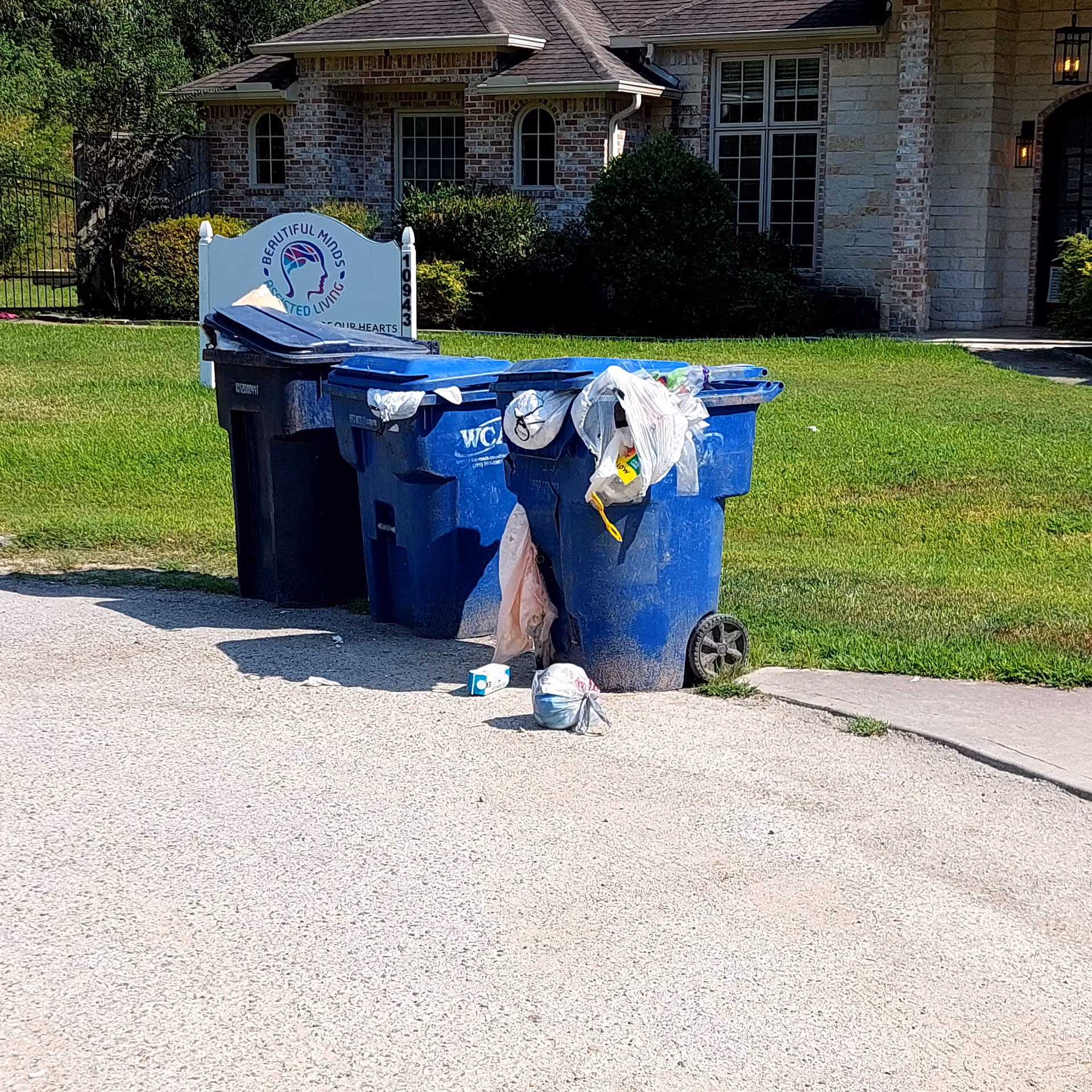 Front of a senior living facility with blue trash bins by the curb.
