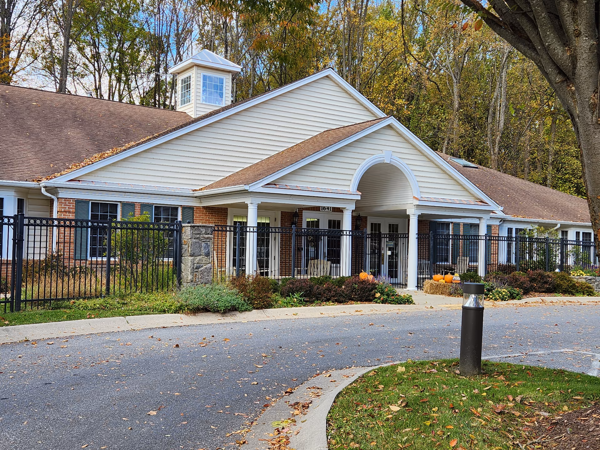 Meadows 1639 senior living facility front with arch entrance, pumpkins, and fence.