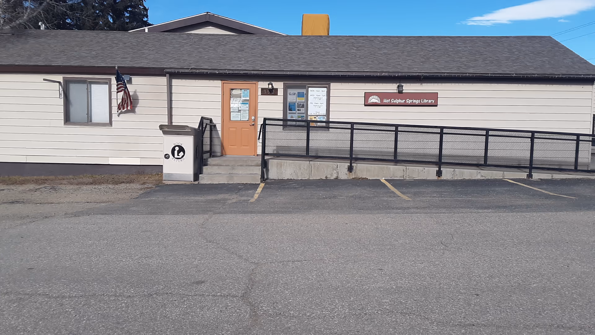 Single-story exterior with ramp, doorway, and Hot Sulphur Springs Library sign in parking lot.