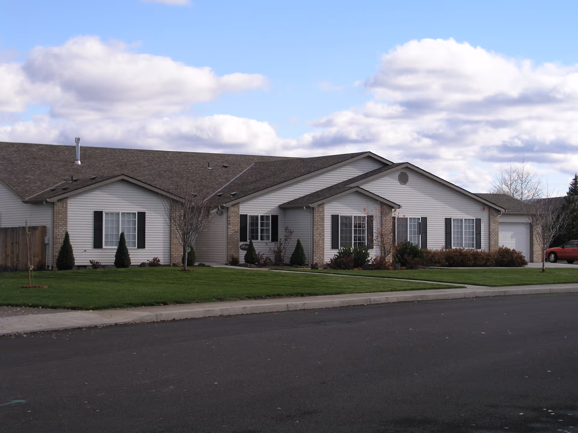 Single-story white residential building with a dark roof, landscaped front lawn and cloudy sky overhead.