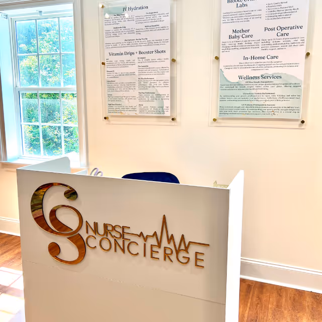 Indoor reception desk with Nurse Concierge logo, wall posters, and a window view.