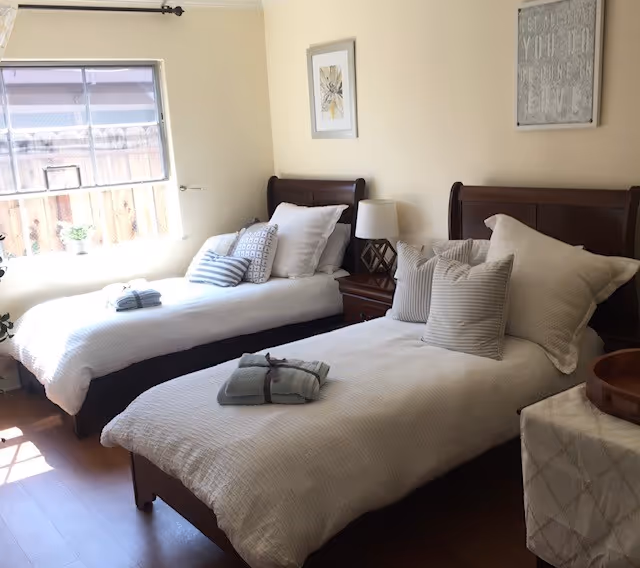 Two single beds with white bedding and pillows in a bright, tidy bedroom.