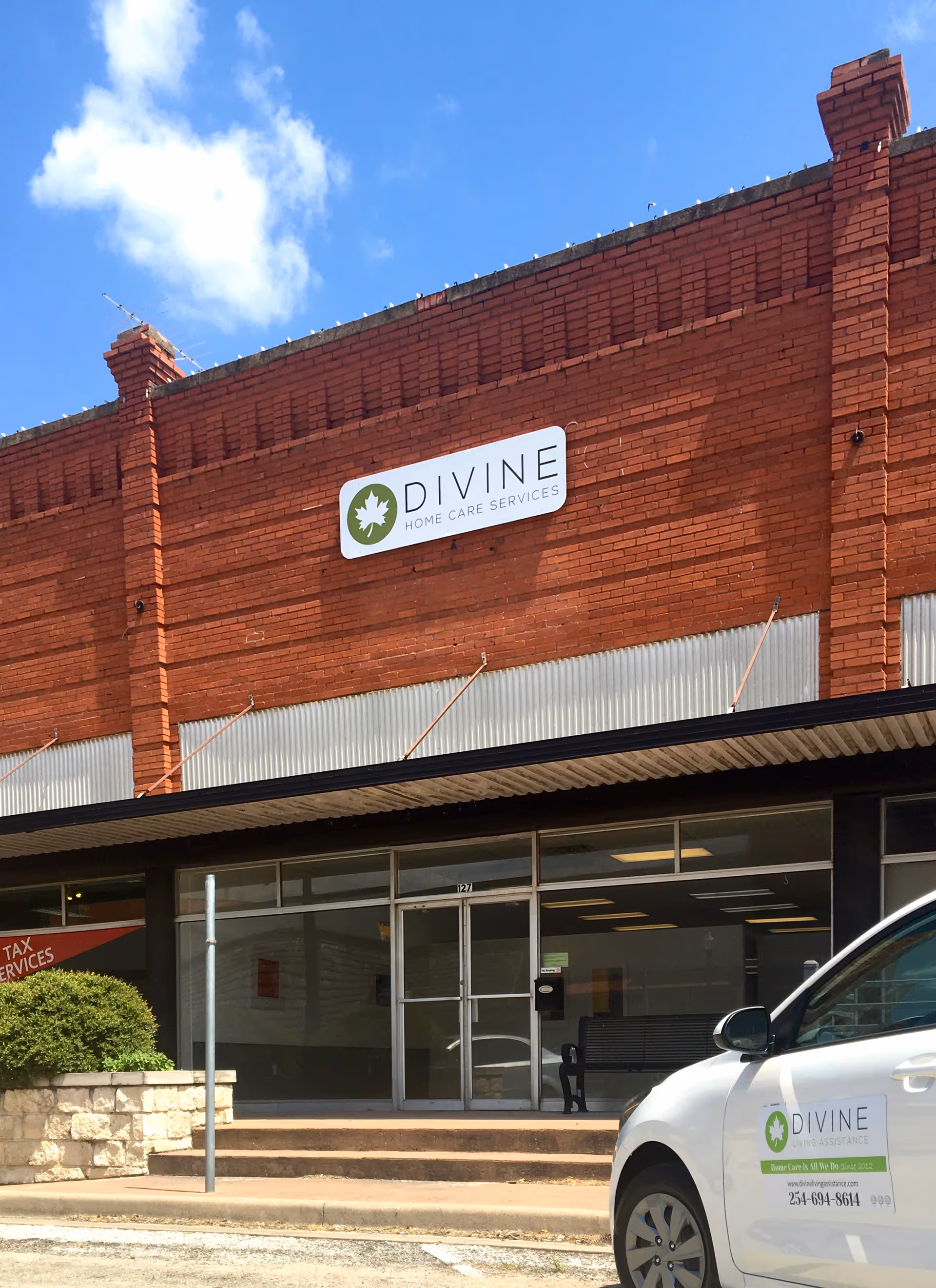 Brick building with Divine Home Care Services sign and a white car parked out front.