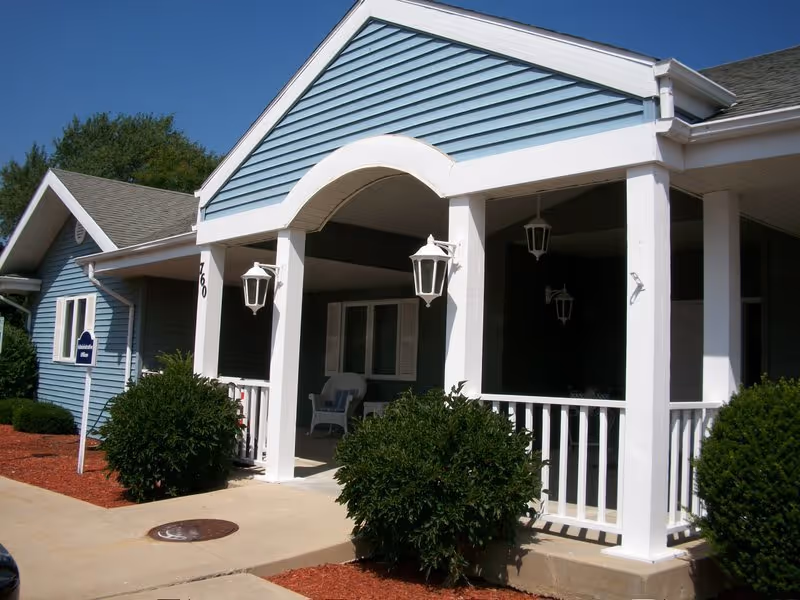 Blue senior living facility exterior with arched porch, white railings, and hanging lamps.