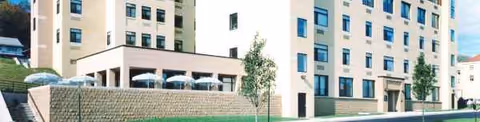 Exterior view of a beige multi-story senior living building with trees and windows.