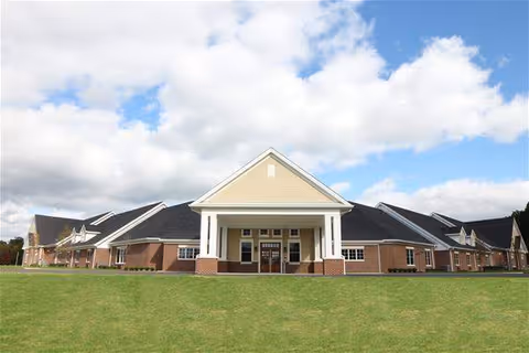 Front exterior of Champion Estates Assisted Living with brick building, green lawn, and blue sky.