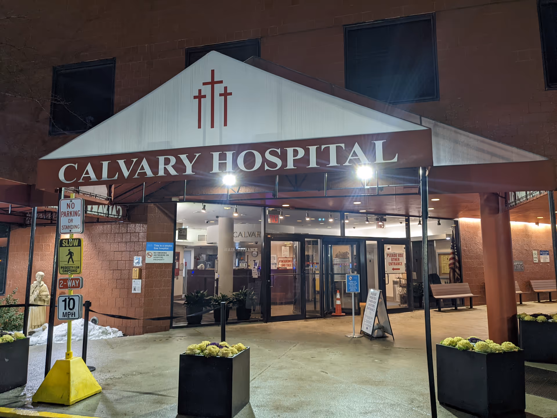 Exterior hospital entrance with Calvary Hospital sign, glass doors, and potted planters under a canopy.