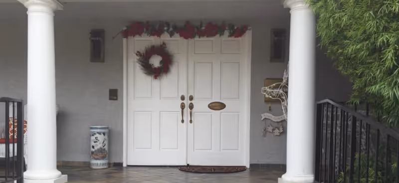 White double doors with a wreath, framed by a covered entry and two columns.