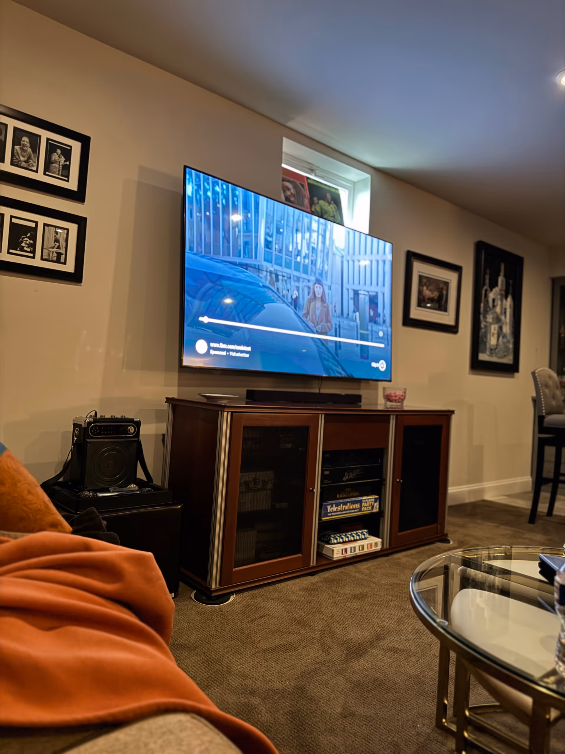 Living room with mounted TV, wooden cabinet, framed art, and glass coffee table.