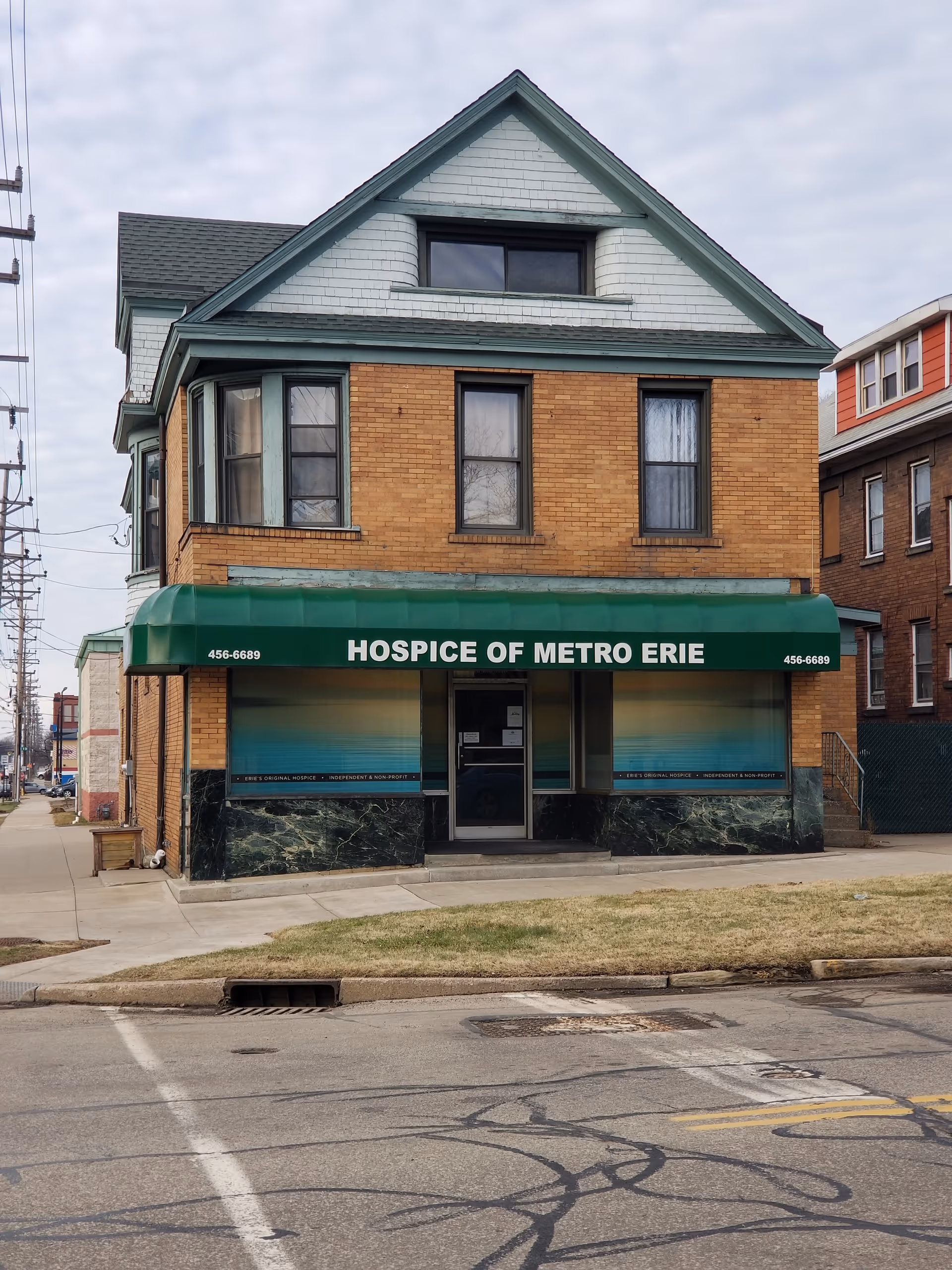 Two-story brick hospice building with green awning reading Hospice of Metro Erie on the storefront.