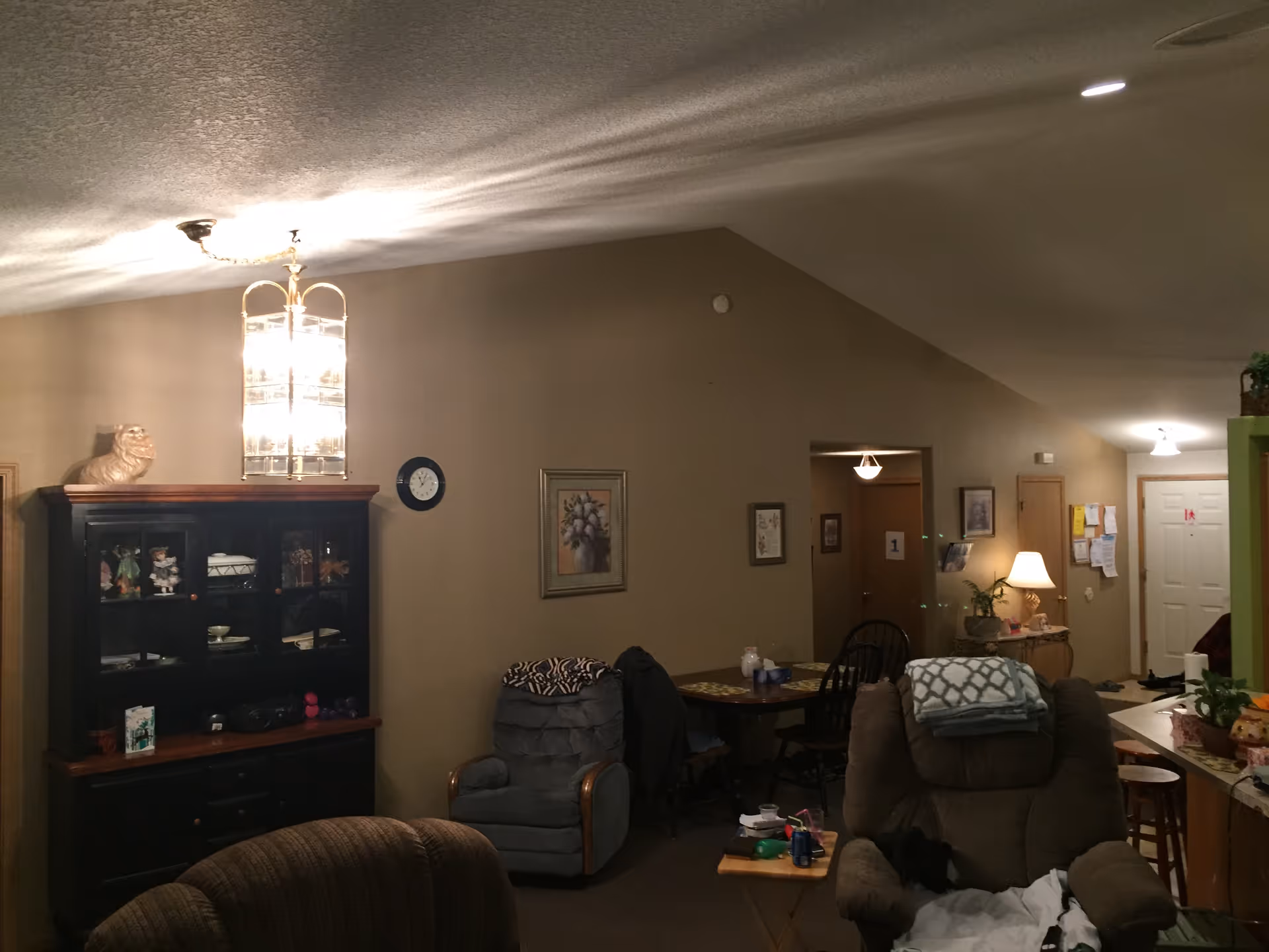 Cozy living room with recliners, a wooden cabinet, and a dining table in warm lighting.