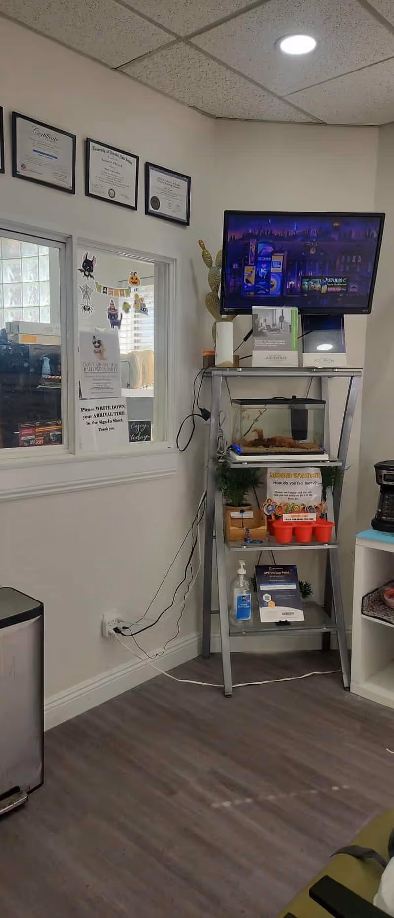 TV mounted above a metal shelf with a small aquarium and pamphlets in a clinic room.