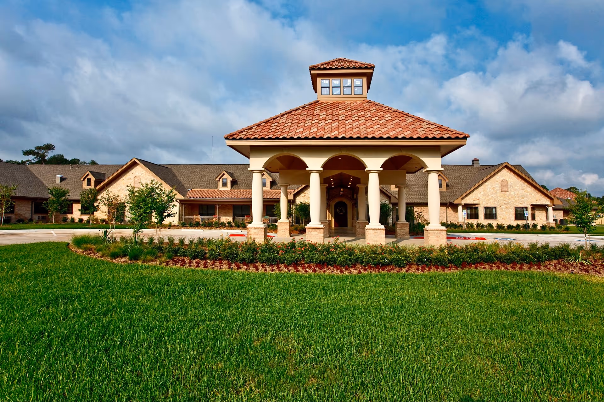 A beige senior living facility with a tiled porte-cochere and lawn.